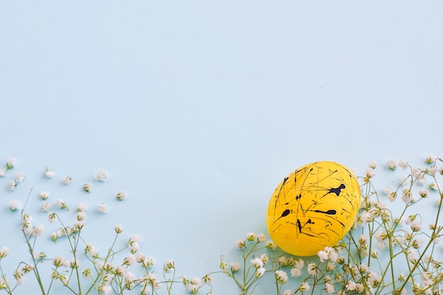 1つの卵は黄色で 水色の背景に黒い斑点と花があり スペースのコピーがあります イースター ミニマリズム お祭りの背景 はがき フレーム プレミアム写真