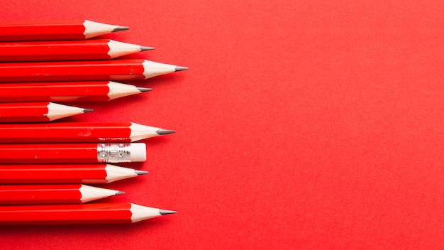 One pencil standing out from other sharp pencils on red backdrop Free Photo