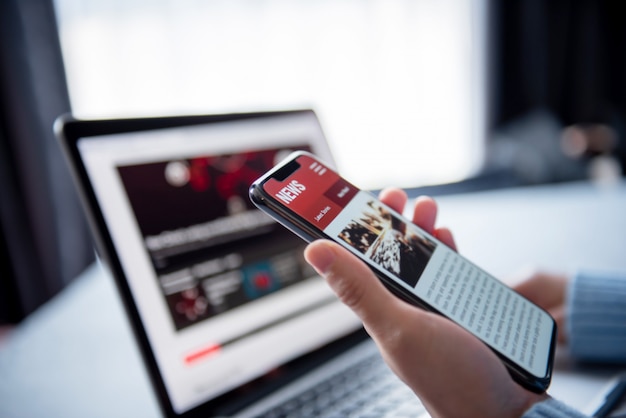 Premium Photo | Online news on a smartphone and laptop. mockup website.  woman reading news or articles in a mobile phone screen application at  home. newspaper and portal on internet.