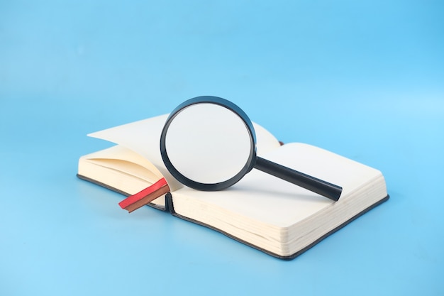 Premium Photo | Open book and magnifying glass on blue background