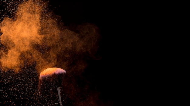 Orange cloud of powder and makeup brush on dark background Free Photo