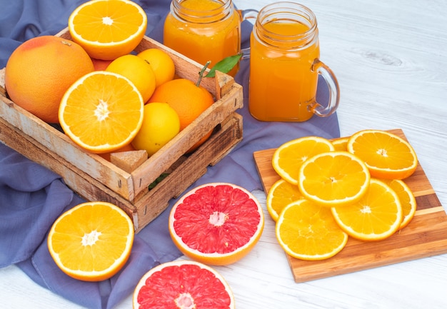 Free Photo Oranges And Lemons In The Wooden Box In Front Of Glasses Of Orange Juice On Violet Cloth
