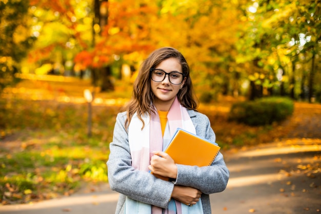 Outdoor autumn portrait happy smiling teenage girl with copybooks Free Photo