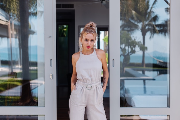 Outdoor portrait of caucasian woman in classic jumpsuit with red lipstick on vacation outside villa hotel Free Photo