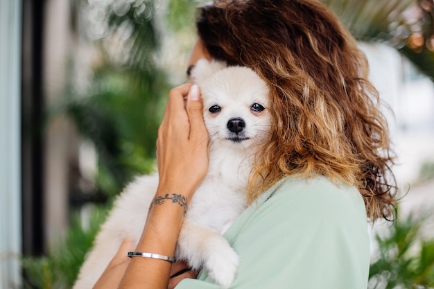 巻き毛のヨーロッパの日焼けした女性の屋外の肖像画は幸せなペットの犬のポメラニアンスピッツを保持します 無料の写真