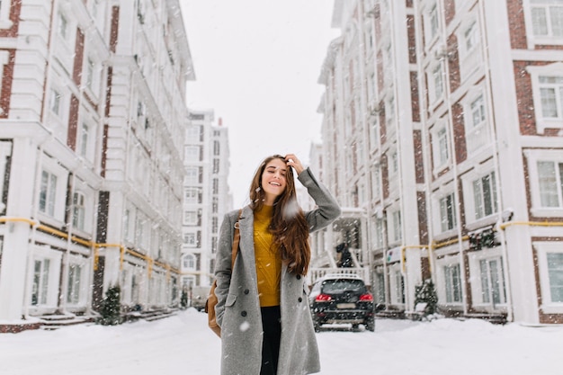 雪の日に買い物に行くトレンディなグレーのコートを着た髪の長い女性の屋外のポートレート 冬の週末に市で過ごすスタイリッシュな服装でゴージャスなブロンドの女性 無料の写真