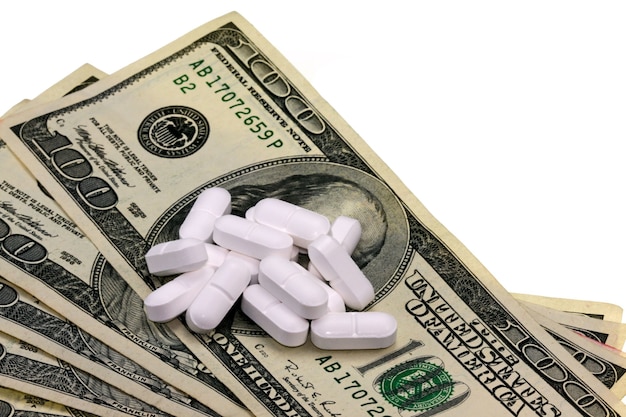 Overhead shot of white tablets placed at the top of a dollar bill with a white background Free Photo