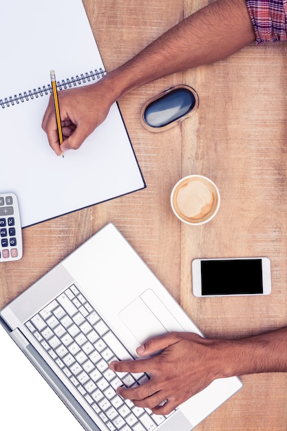 Overhead view of businessman working on laptop while writing on book at desk in office Premium Photo