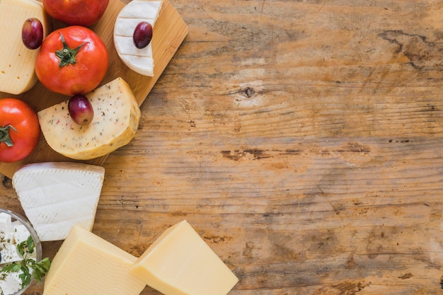 An overhead view of cheese blocks, grapes and tomatoes on wooden desk Free Photo