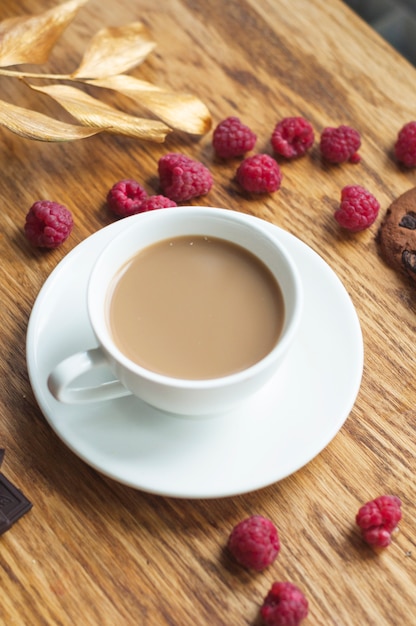 An overhead view of coffee cup on saucer with fresh raspberries on wooden table | Free Photo