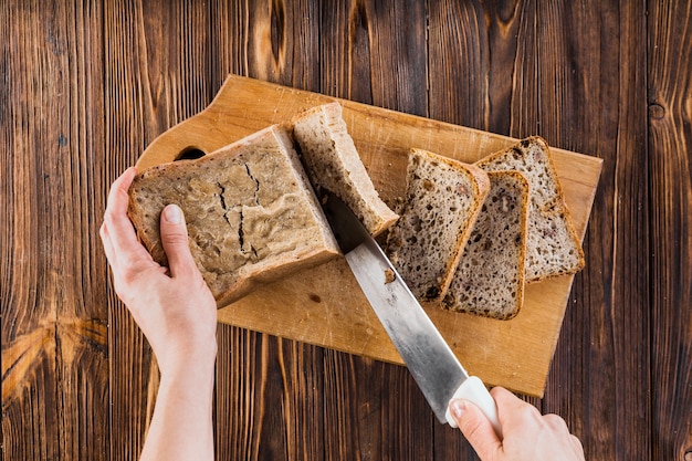 Overhead view of cutting bread with sharp knife on wooden board | Free  Picture on Freepik