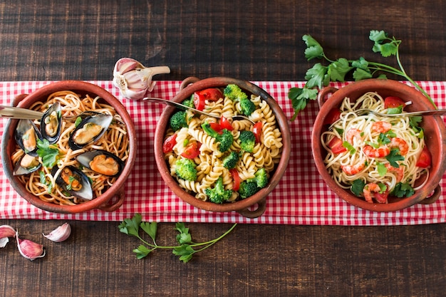 An overhead view of earthenware with different type of pasta on tablecloth Free Photo