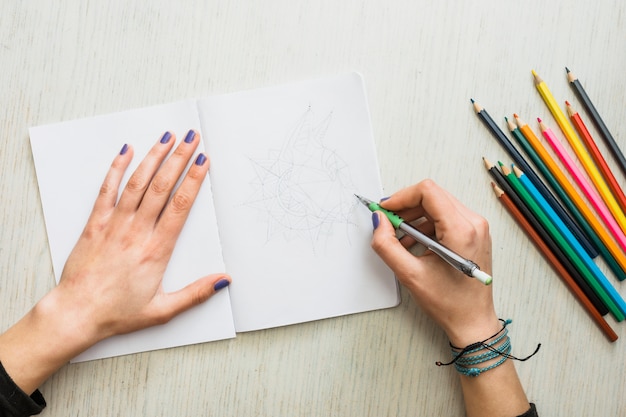 Overhead view of human's hand sketching on white drawing book | Free Photo