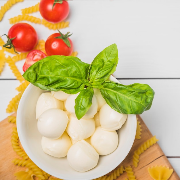 An overhead view of italian mozzarella cheese with basil leaf; tomatoes and fusilli pasta Free Photo