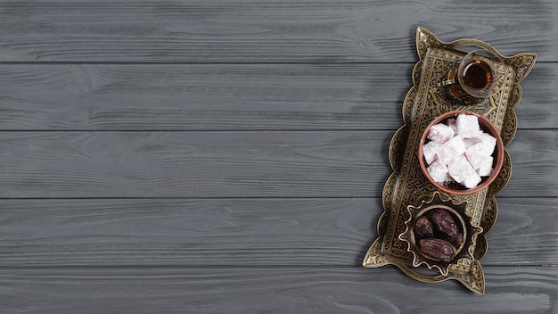 An overhead view of metallic tray with turkish delight lukum; dates and tea on ramadan over the wooden table Free Photo