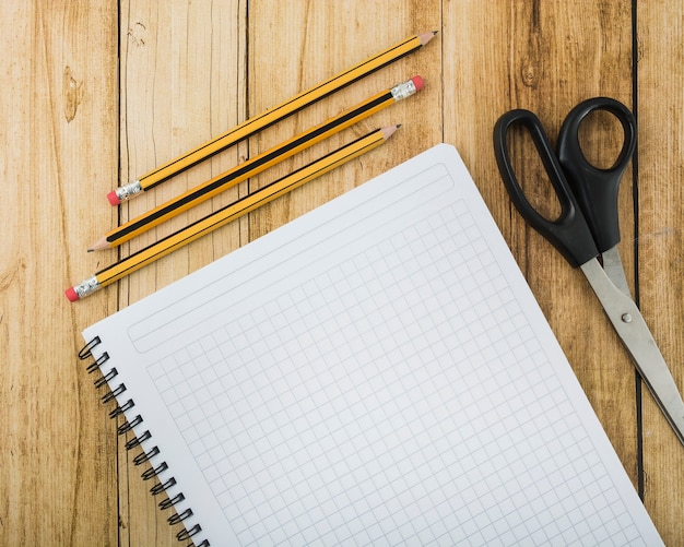 Overhead view of notepad; scissors and pencils on wooden plank Free Photo