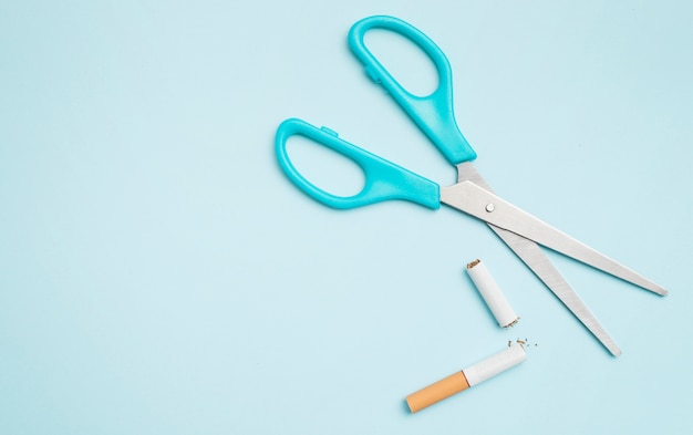 Overhead view of scissor and broken cigarette on colored background Free Photo