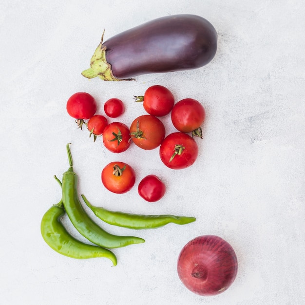 An overhead view of tomatoes; green chilies; onion and eggplant on white textured background Free Photo
