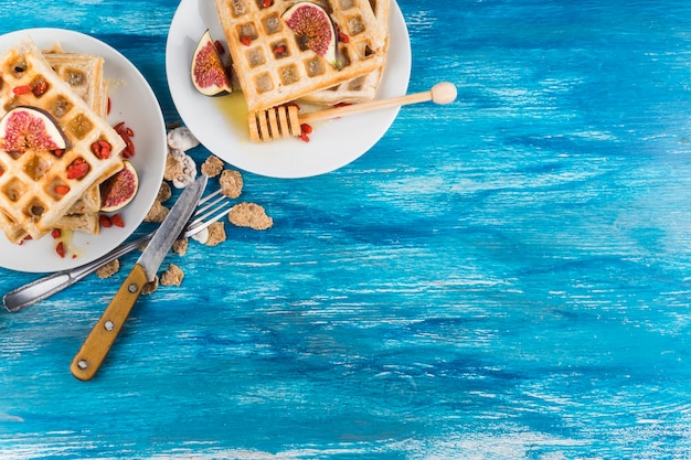 An overhead view of waffles with fig slices on plate against wooden blue textured background Free Photo
