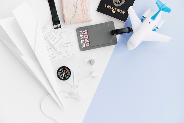 An overhead view of world traveler tag with passport; paper airplane; map; compass; tickets; toy airplane and earphone on dual background Free Photo