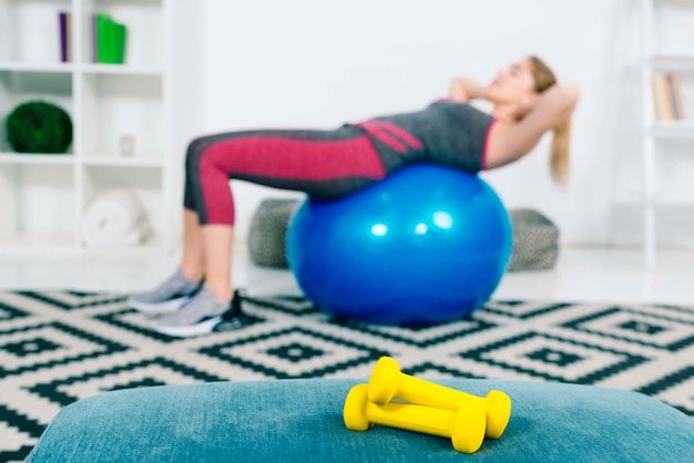 Pair of yellow dumbbells in front of woman exercising on blue pilates ball Free Photo