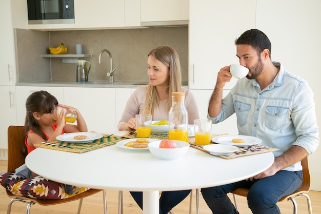 Free Photo | Parents and kid enjoying breakfast together, drinking coffee  and orange juice, sitting at dining table with fruits and cookies and  talking.