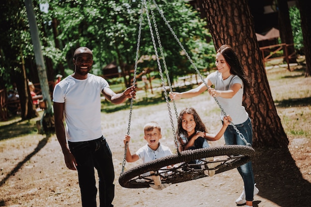 Premium Photo Parents Pushing Swing For Happy Children In Park