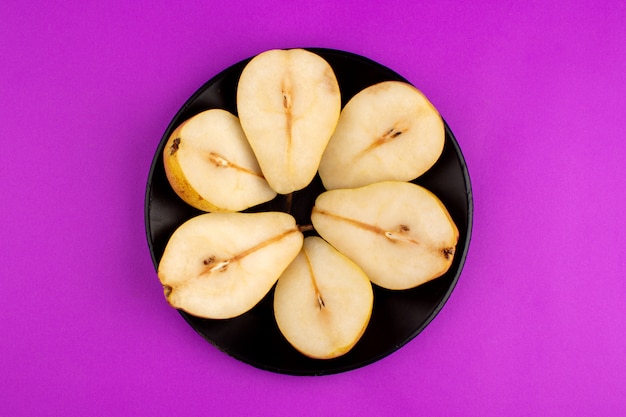 梨の丸い形の紫色の机の上の黒い皿の中の新鮮な熟した果物 無料の写真