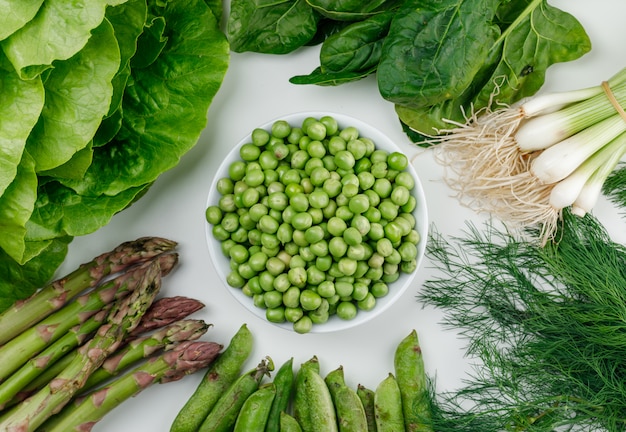 Peas with lettuce, asparagus, green pods and onion, dill, sorrel in a white bowl on white wall, top view. Free Photo