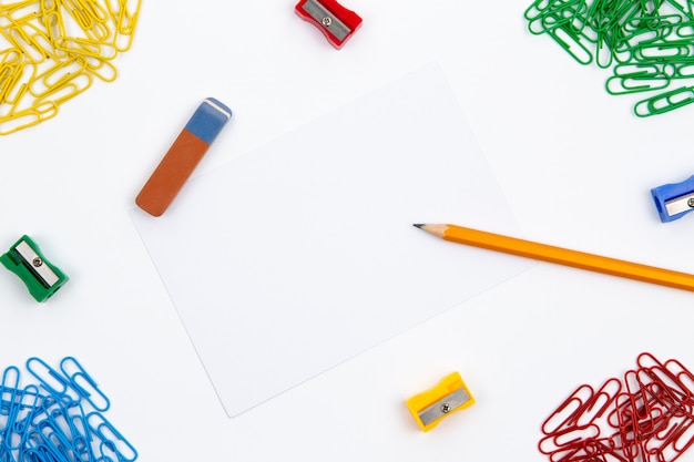 Pencil, eraser, sharpener, paper clips lie in different angles of the sheet on a white background. hero image and copy space. Premium Photo