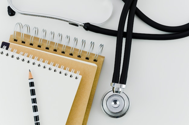 Pencil on the stack of spiral notepad with stethoscope on white backdrop Free Photo