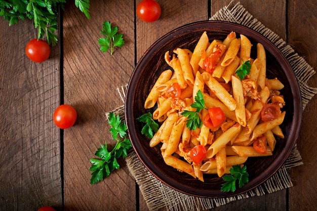 Penne pasta in tomato sauce with chicken and tomatoes on a wooden table Free Photo