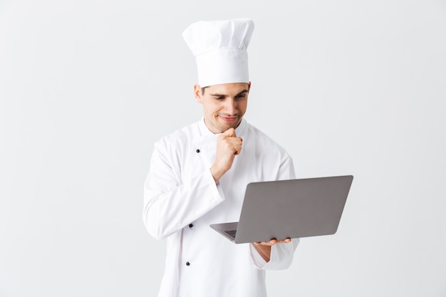 Premium Photo Pensive Chef Cook Wearing Uniform Standing Over White Wall Holding Laptop Computer