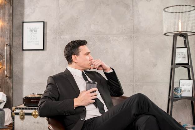 Pensive man holding cup of coffee in room Free Photo