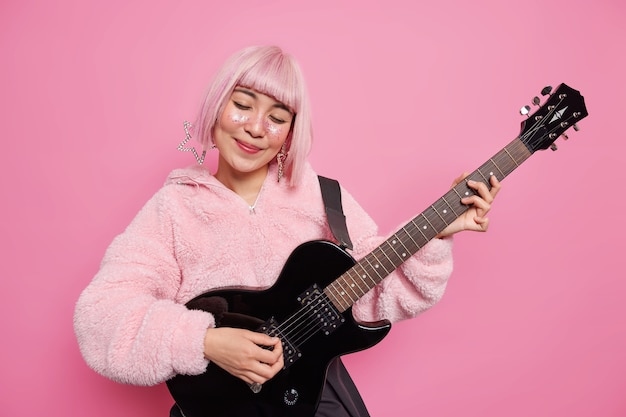 人々の趣味の音楽の概念 満足のいくスタイリッシュなピンクの髪の才能のある女性ミュージシャンがアコースティックギターでロックンロールの曲を演奏し 人気のスターであるステージで演奏します 無料の写真
