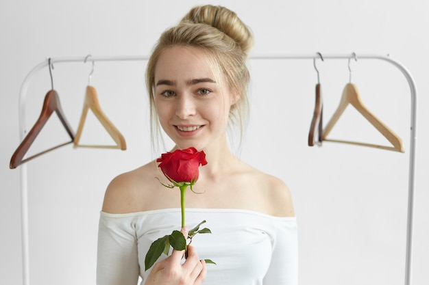 人々 愛 ロマンス 美しさと愛情の概念 彼女の未知の秘密の崇拝 者からの1つの赤いバラを持って 笑顔で 白いオープンショルダートップを身に着けている魅力的な若い白人女性 無料の写真