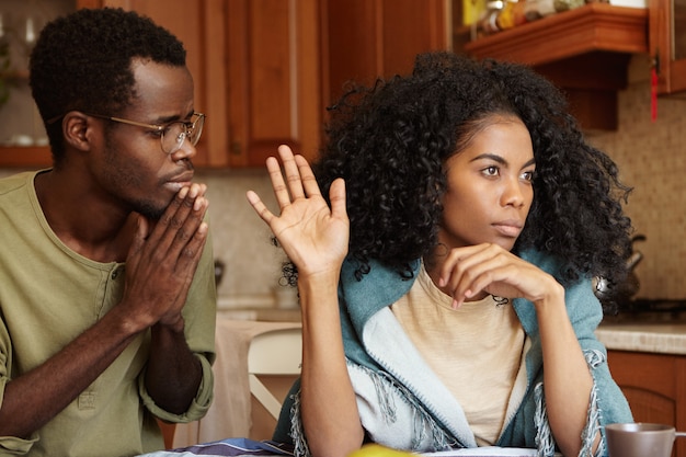 People, relationships problems and divorce. repentant worried dark-skinned male keeping hands pressed together, begging offended wife to forgive his infidelity, mad woman not looking at him at all Free Photo