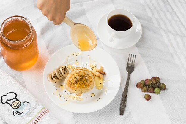 A person adding honey on pancake with wooden spoon Free Photo