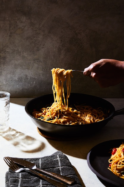Person getting some spaghetti from a black pot on a white table