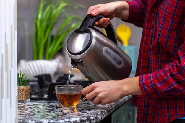 Premium Photo A Person Makes Tea Using Boiling Water From An Electric Kettle In Kitchen At