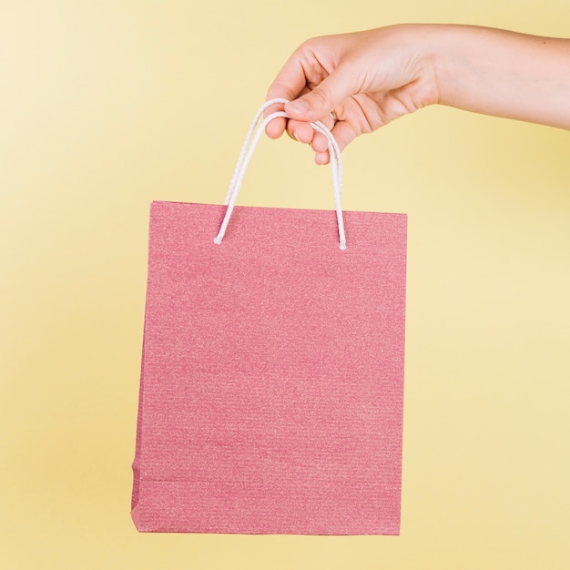 Download Free Photo A Person S Hand Holding Pink Paper Shopping Bag On Yellow Background PSD Mockup Templates