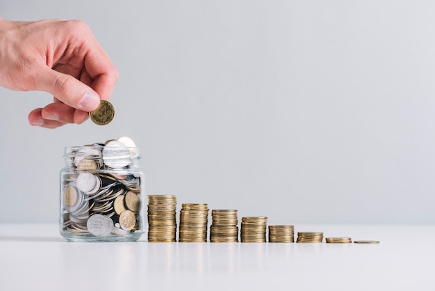 A person's hand putting money in glass jar near decreasing stacked coins Free Photo