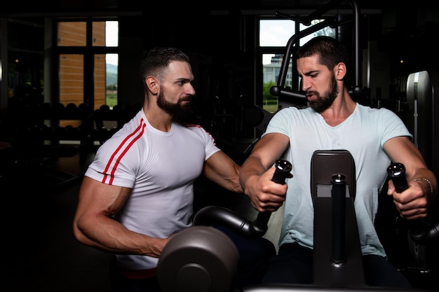 Premium Photo | Personal trainer showing young man how to train back on ...