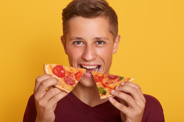 2枚のピザを保持し ファーストフードを食べるバーガンディのtシャツを着た男の写真 無料の写真