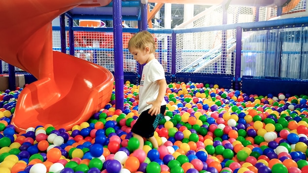 かっこいいプラスチックボールでいっぱいのプールで遊んでいる男の子の写真 ショッピングモールの遊び場で楽しんでいる幼児 プレミアム写真