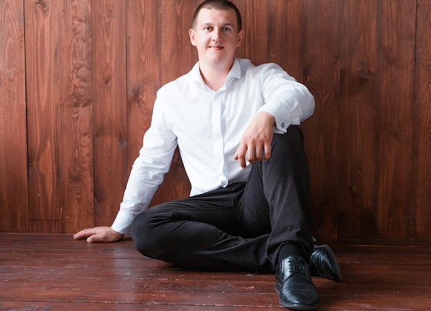 ズボンとシャツの男の写真は床に座って 木製の壁の背景にポーズ プレミアム写真