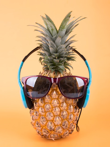 オレンジ色の背景にサングラスとヘッドホンを持つパイナップル フルーツサマーコンセプト プレミアム写真