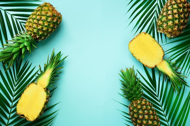 Pineapples and tropical palm leaves on punchy pastel turquoise background. summer concept. creative flat lay with copy space. Premium Photo