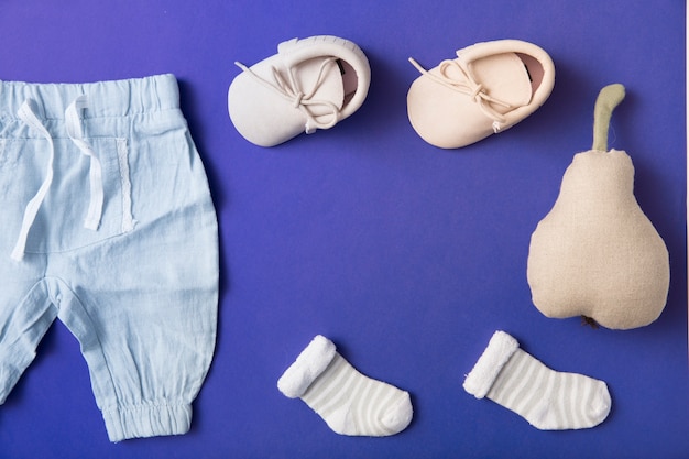 Pink baby shoes; sock and baby's pant with stuffed pear on bright blue background Free Photo