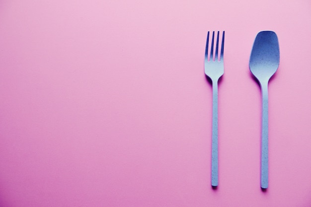 Plastic blue spoon and fork on pink background | Premium Photo